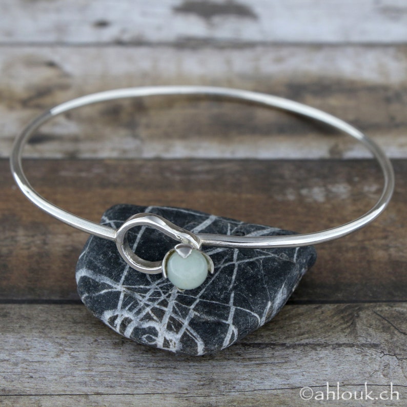 May include: A silver bangle bracelet with a light green stone accent. The bracelet is open and has a simple design.
