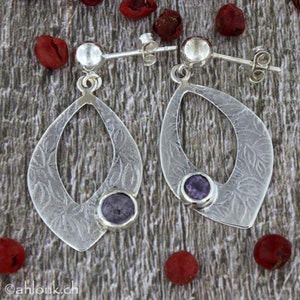 May include: A pair of silver dangle earrings with a textured leaf design and a purple gemstone in the center of each earring.