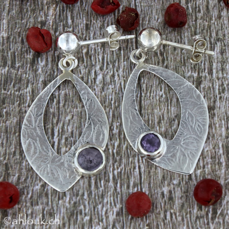 May include: A pair of silver dangle earrings with a textured leaf design and a purple gemstone in the center of each earring.