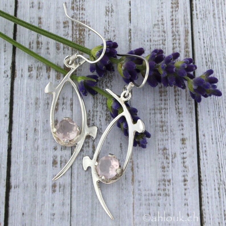 Pu&ograve; includere: Orecchini d'argento con un design delicato e astratto che presenta una pietra preziosa rosa in ogni orecchino.