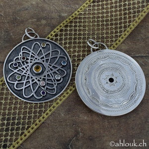 May include: Two silver pendants, one with a circular design and the other with a stylized atom design with colorful gemstones.