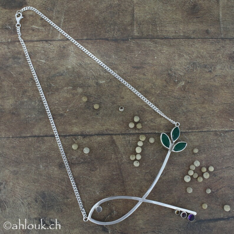May include: A silver necklace with a fish pendant and a green leaf design. The pendant has a small cluster of colorful gemstones.