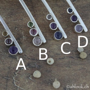 May include: Five silver bar pendants with different colored gemstones. The pendants are labeled A, B, C, and D. The gemstones are purple, green, pink, and clear.