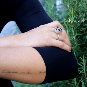 May include: A silver ring with a black geometric design. The ring is worn on a person's finger.