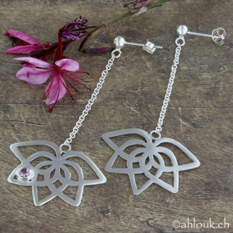 May include: A pair of silver dangle earrings with a delicate chain and a floral design. One earring features a small pink gemstone in the center of the flower.