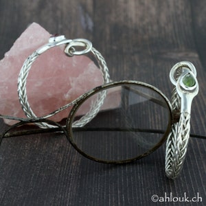 May include: Two silver bracelets with braided chain designs. One bracelet features a red gemstone, the other a green gemstone.