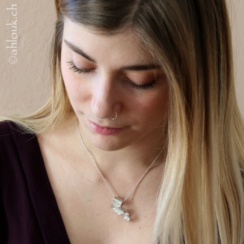 May include: A silver necklace with a textured, abstract pendant. The pendant is shaped like a cluster of leaves or flowers.