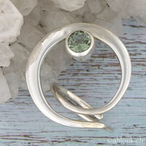 May include: A silver ring with a green gemstone set in a crescent moon design.