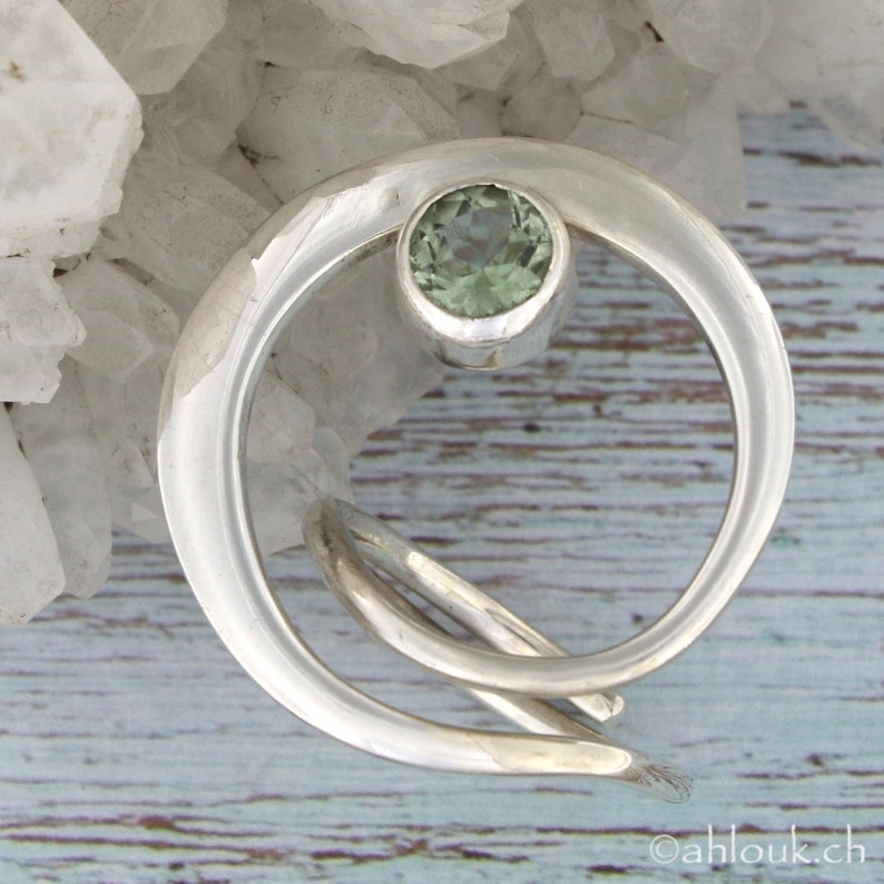 May include: A silver ring with a green gemstone set in a crescent moon design.