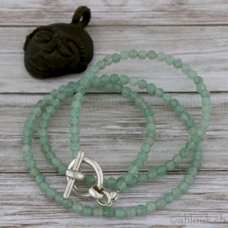 May include: A green jade necklace with a silver toggle clasp. The necklace is made of small, round beads and is approximately 18 inches long.
