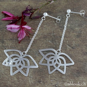 May include: A pair of silver dangle earrings with a delicate chain and a floral design. One earring features a clear crystal in the center of the flower.
