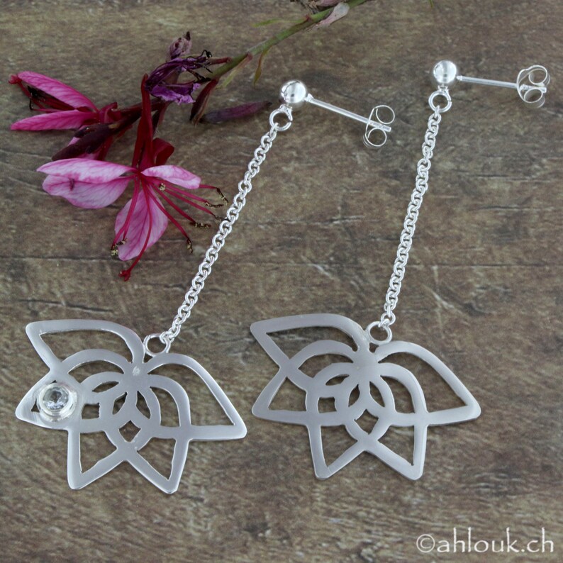 May include: A pair of silver dangle earrings with a delicate chain and a floral design. One earring features a clear crystal in the center of the flower.