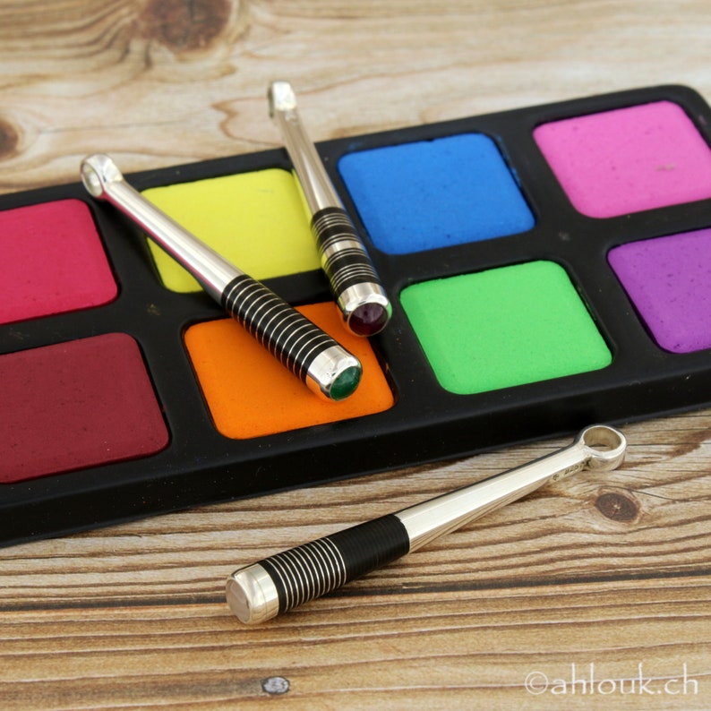 May include: Three silver and black striped sticks with colorful gemstones on the ends. The sticks are resting on a black and colorful paint palette.