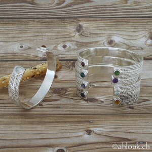 Puede incluir: Cinco pulseras de plata con piedras preciosas de diferentes colores. Cada pulsera tiene un dise&ntilde;o trenzado y una sola piedra preciosa engastada en el metal. Las piedras preciosas son roja, verde, morada, azul y naranja.
