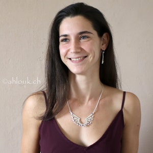 May include: A woman wearing a burgundy tank top with a silver necklace featuring a wing design with purple accents.