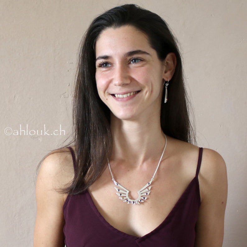 May include: A woman wearing a burgundy tank top with a silver necklace featuring a wing design with purple accents.