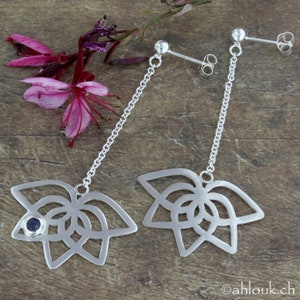 May include: A pair of silver dangle earrings with a delicate chain and a geometric flower design. One earring features a small blue gemstone in the center of the flower.