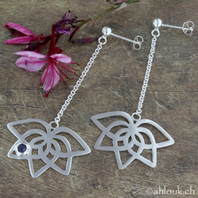 May include: A pair of silver dangle earrings with a delicate chain and a geometric flower design. One earring features a small blue gemstone in the center of the flower.