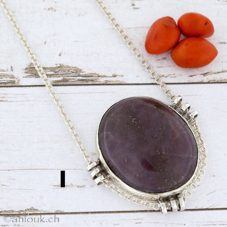 Puede incluir: Un collar de cadena de plata con un gran colgante ovalado con una piedra p&uacute;rpura y gris. El colgante est&aacute; engastado en un marco de plata con detalles decorativos.