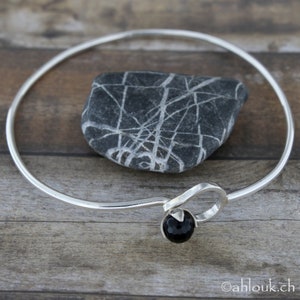 May include: A silver bangle bracelet with a black onyx stone accent. The bracelet is open and has a simple, elegant design.
