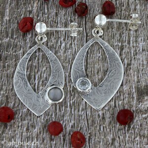 May include: A pair of silver earrings with a teardrop-shaped design. Each earring features a small, clear stone set in the center of the teardrop. The earrings have a textured surface and are accented with a small, round silver bead at the top.