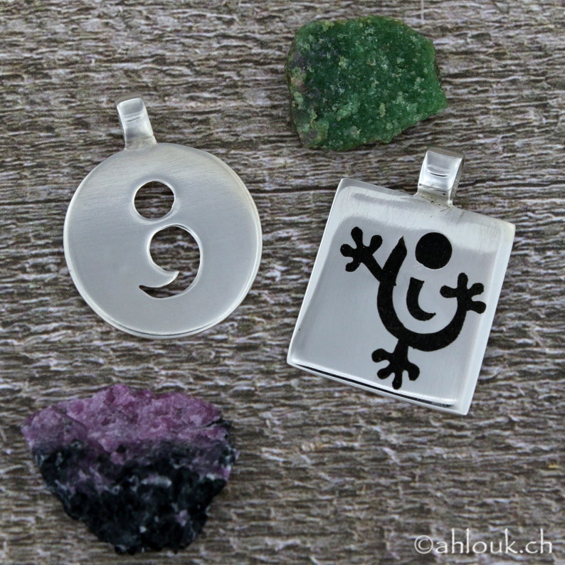 May include: Two silver pendants, one with a semicolon cutout and the other with a stylized black figure with a circle head and outstretched arms.