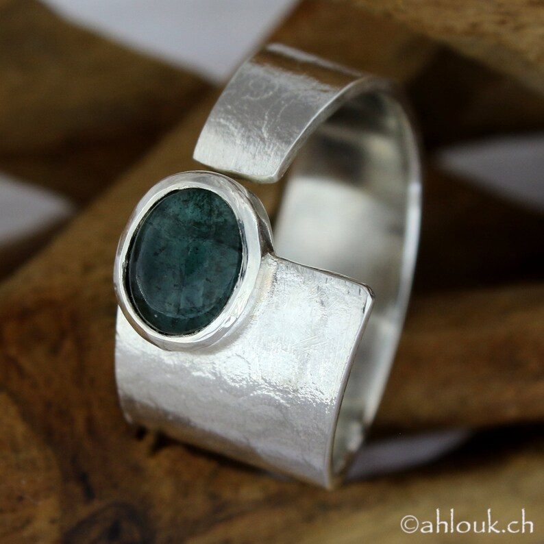 May include: A silver ring with a textured finish and a green gemstone set in a bezel setting.