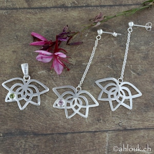 May include: A set of silver earrings and a pendant featuring a delicate, openwork lotus flower design with a small gemstone in the center. The earrings are drop earrings with a chain and the pendant has a loop for a chain.