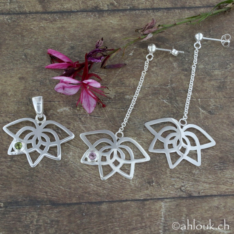 May include: A set of silver earrings and a pendant featuring a delicate, openwork lotus flower design with a small gemstone in the center. The earrings are drop earrings with a chain and the pendant has a loop for a chain.