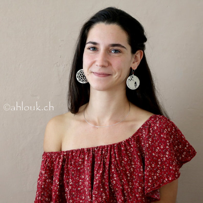 May include: A woman with long dark hair wearing a red floral off-the-shoulder top and silver earrings. The earrings are round and feature a delicate floral design.