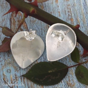 May include: A pair of silver teardrop-shaped earrings with a post back closure. The earrings are marked with the letter "R" on the back.