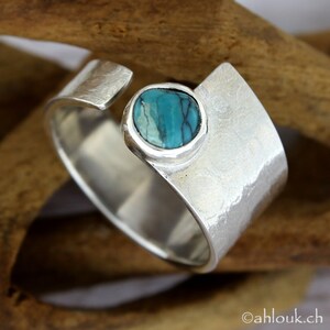 May include: A silver ring with a turquoise stone set in a bezel. The ring is hammered and has a textured finish.