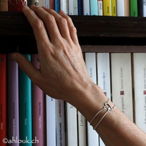 May include: A silver bracelet with a heart-shaped charm on a bookshelf with a variety of books.