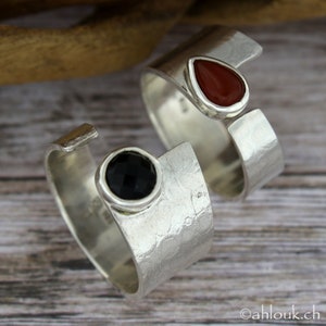 May include: Two silver rings with open bands. One ring has a black gemstone and the other has a red gemstone.