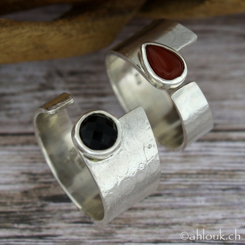May include: Two silver rings with open bands. One ring has a black gemstone and the other has a red gemstone.