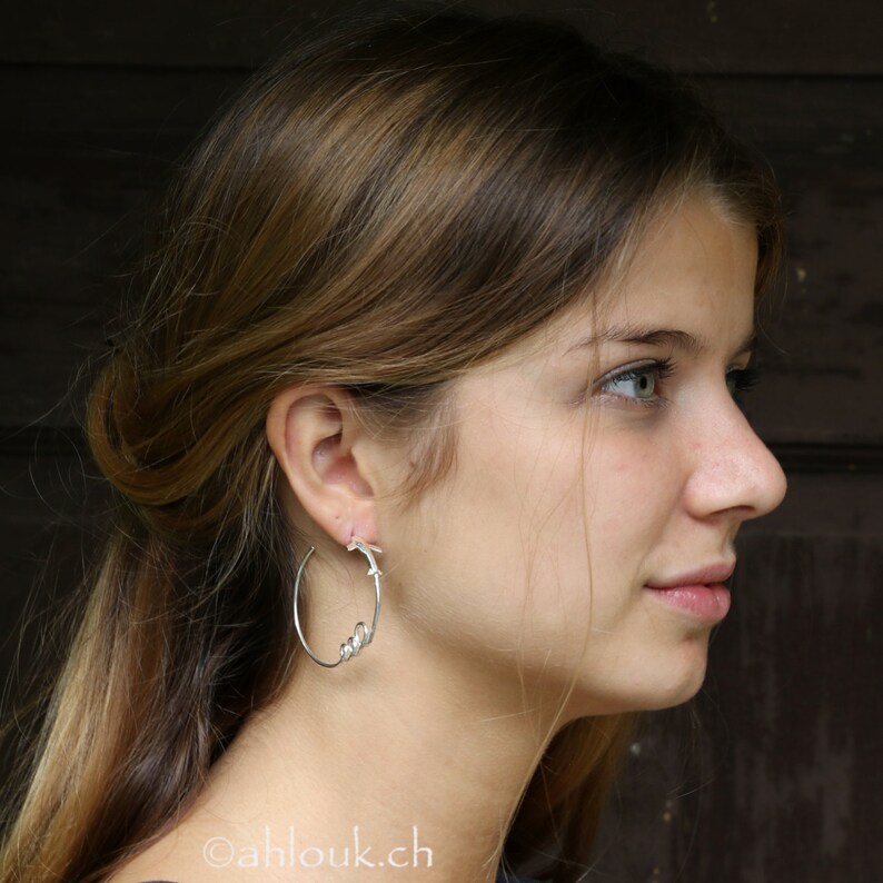 May include: A woman with long brown hair wearing silver hoop earrings with a twisted design. The earrings are visible in her left ear.