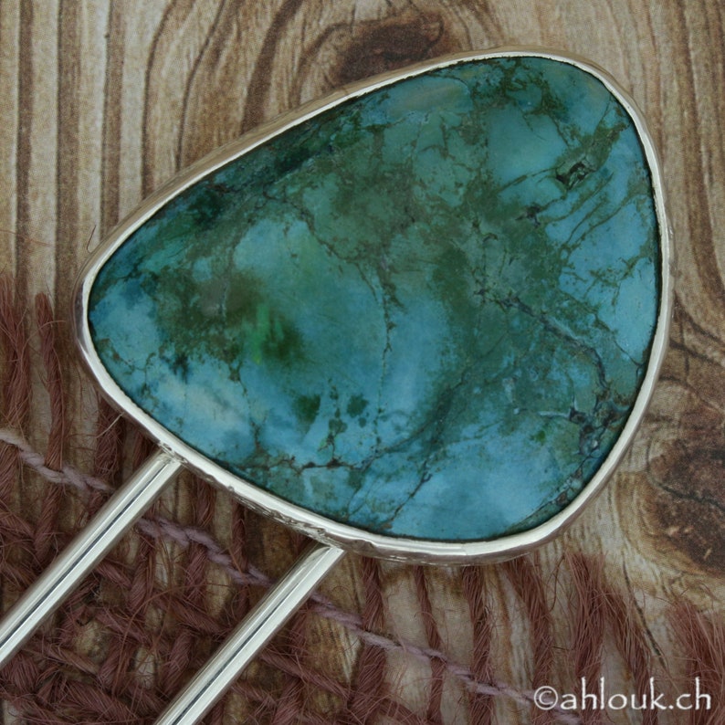 May include: A silver hair fork with a large, green turquoise stone set in the center. The stone has a marbled pattern and is surrounded by a silver border.