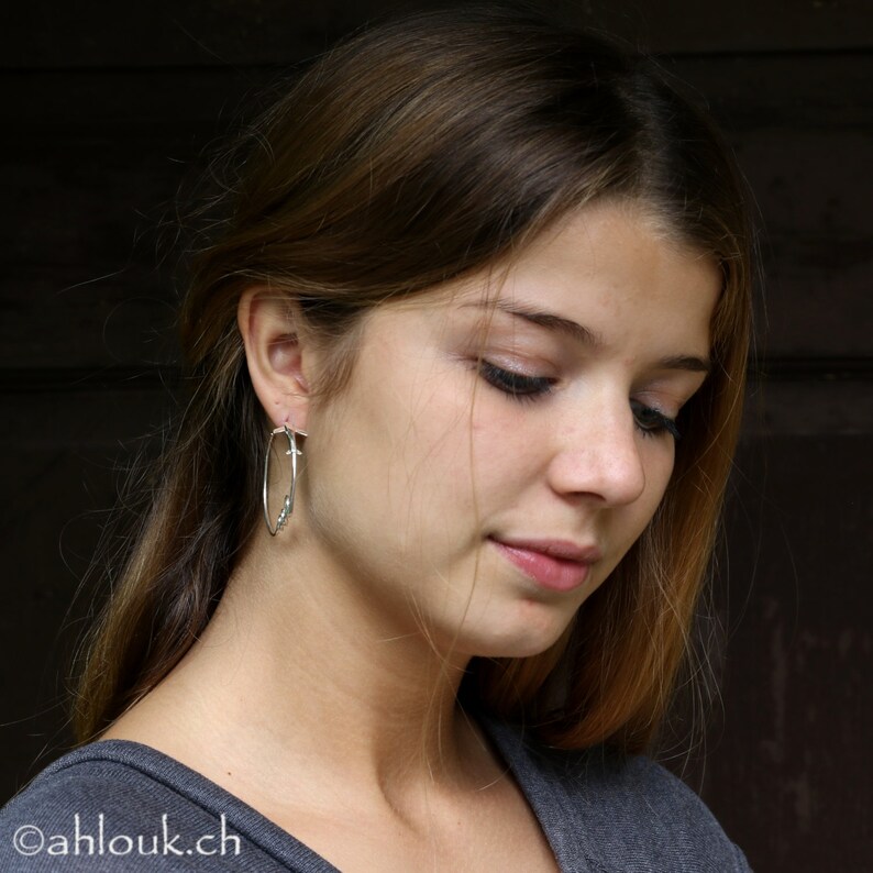 May include: A young woman with long brown hair wearing a gray shirt and silver hoop earrings with small beads.