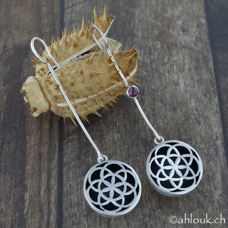 May include: A pair of silver earrings with black and white geometric designs and a small purple gemstone accent.