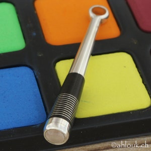 May include: A silver and black metal tool with a ring at the top, resting on a colorful palette of paint squares.