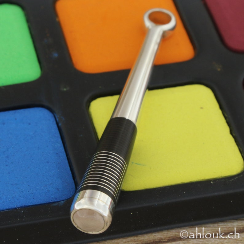 May include: A silver and black metal tool with a ring at the top, resting on a colorful palette of paint squares.