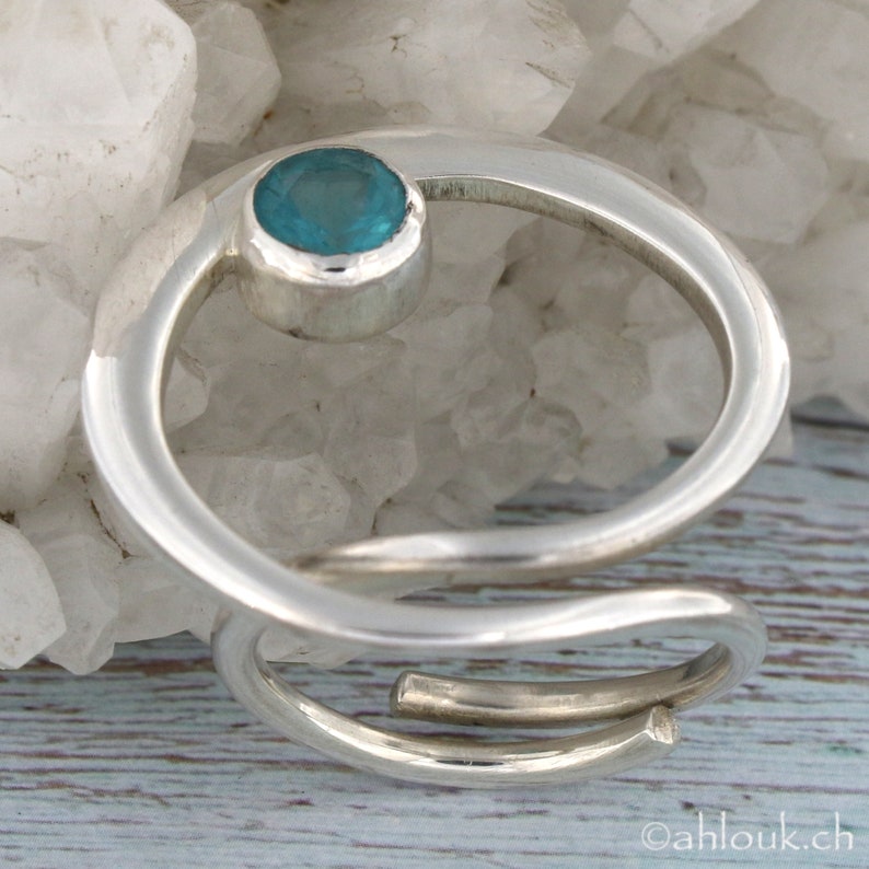 May include: A silver ring with a turquoise gemstone set in a circular bezel. The ring is made of two bands that are twisted together.