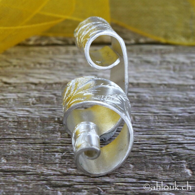 May include: A silver ring with a floral design. The ring is curled into a spiral shape.