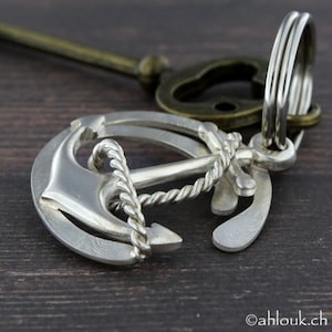 May include: A silver anchor keychain with a rope design. The anchor is detailed with a textured surface and a small ring for attaching keys.
