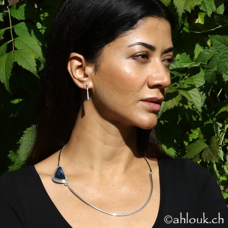 Peut inclure: Un collier en argent avec un pendentif en pierre bleue. Le collier est port&eacute; par une personne aux cheveux fonc&eacute;s et portant une chemise noire.