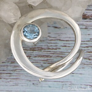May include: A silver ring with a swirling design and a light blue gemstone in the center.