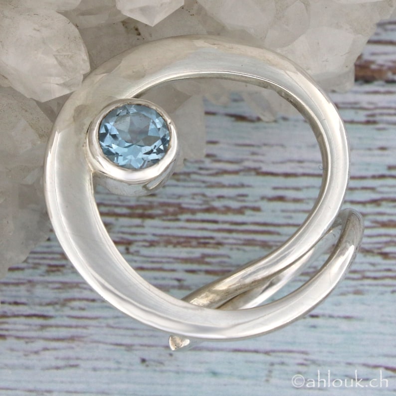 May include: A silver ring with a swirling design and a light blue gemstone in the center.