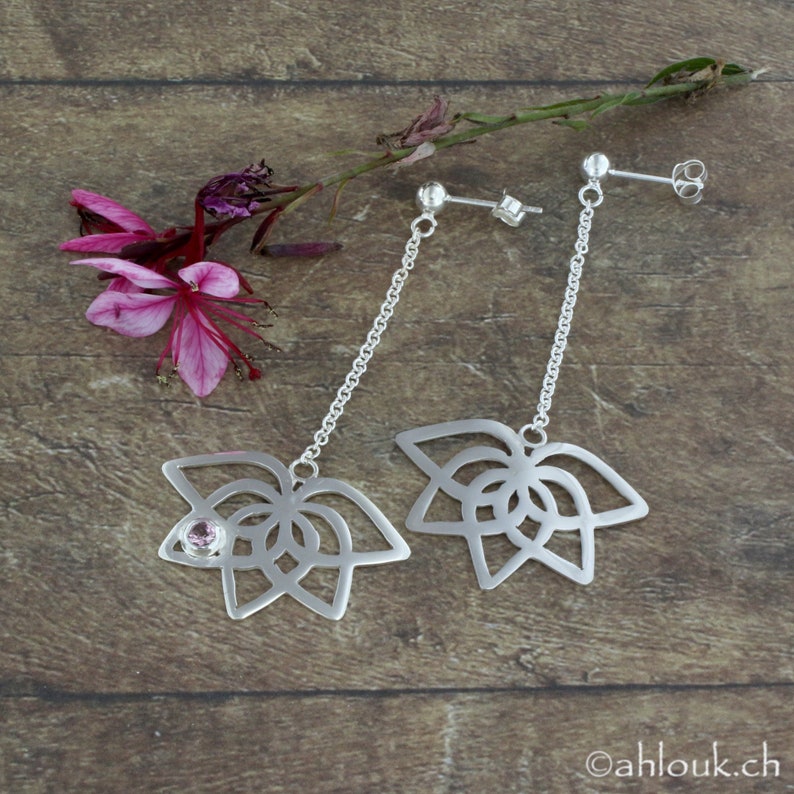 May include: A pair of silver dangle earrings with a delicate chain and a floral design. The earrings feature a small pink gemstone in the center of the floral design.