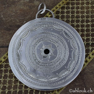May include: Silver pendant with a circular design featuring a star with a hole in the center. The pendant has a detailed, intricate pattern of concentric circles and lines. The back of the pendant is marked with "925".
