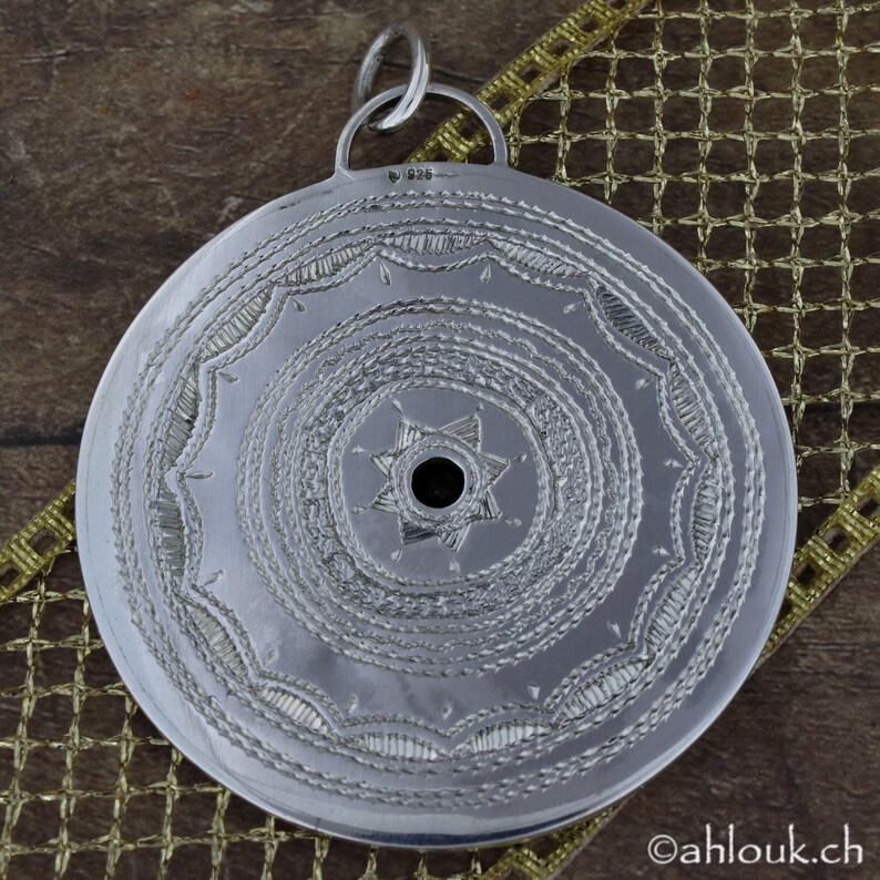 May include: Silver pendant with a circular design featuring a star with a hole in the center. The pendant has a detailed, intricate pattern of concentric circles and lines. The back of the pendant is marked with "925".